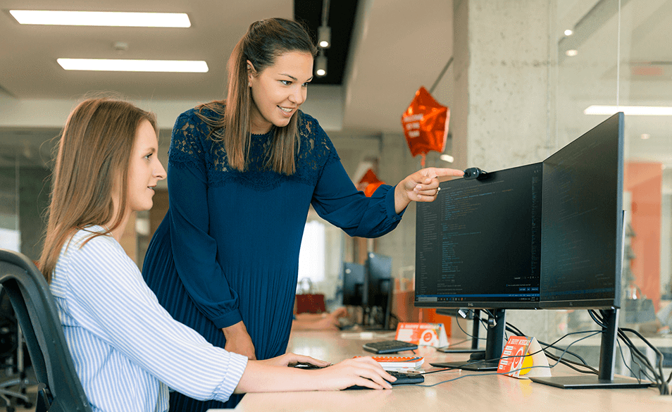 Two colleagues are looking at a computer and talking about a code